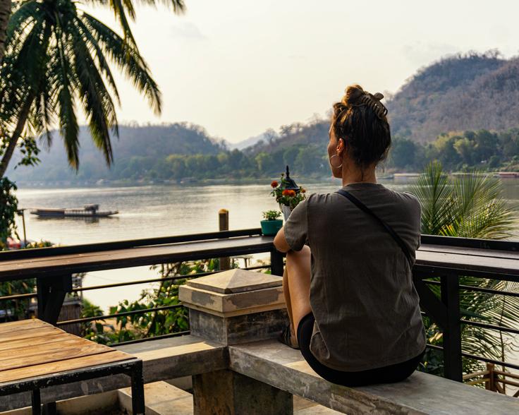 Girl sitting on a bench watching over the Nam Khan river Luang Prabang at sunset